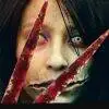 Kuchisake-onna aus dem Film "Carved: The slit mouthed woman", eine blutige Schwere vor ihr geisterhaftes Gesicht haltend.